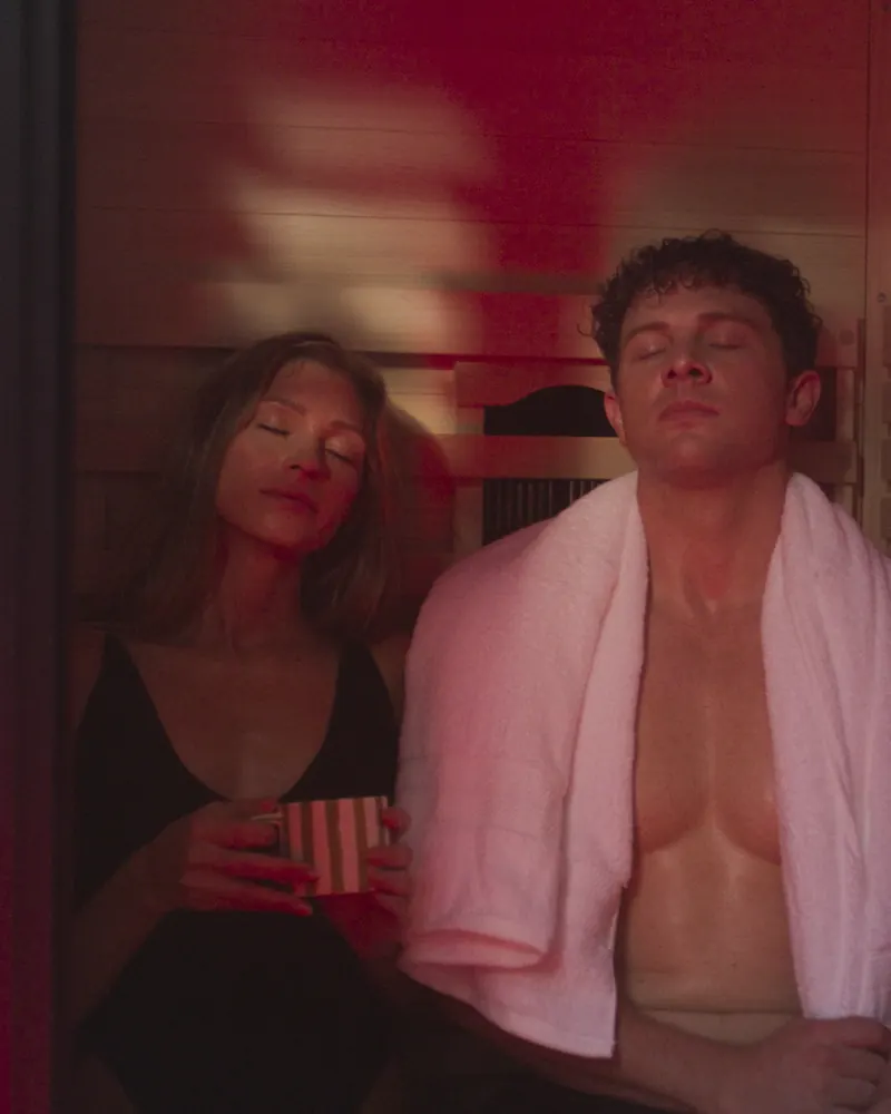 Two people sharing a session inside a PEAK infrared sauna under red light